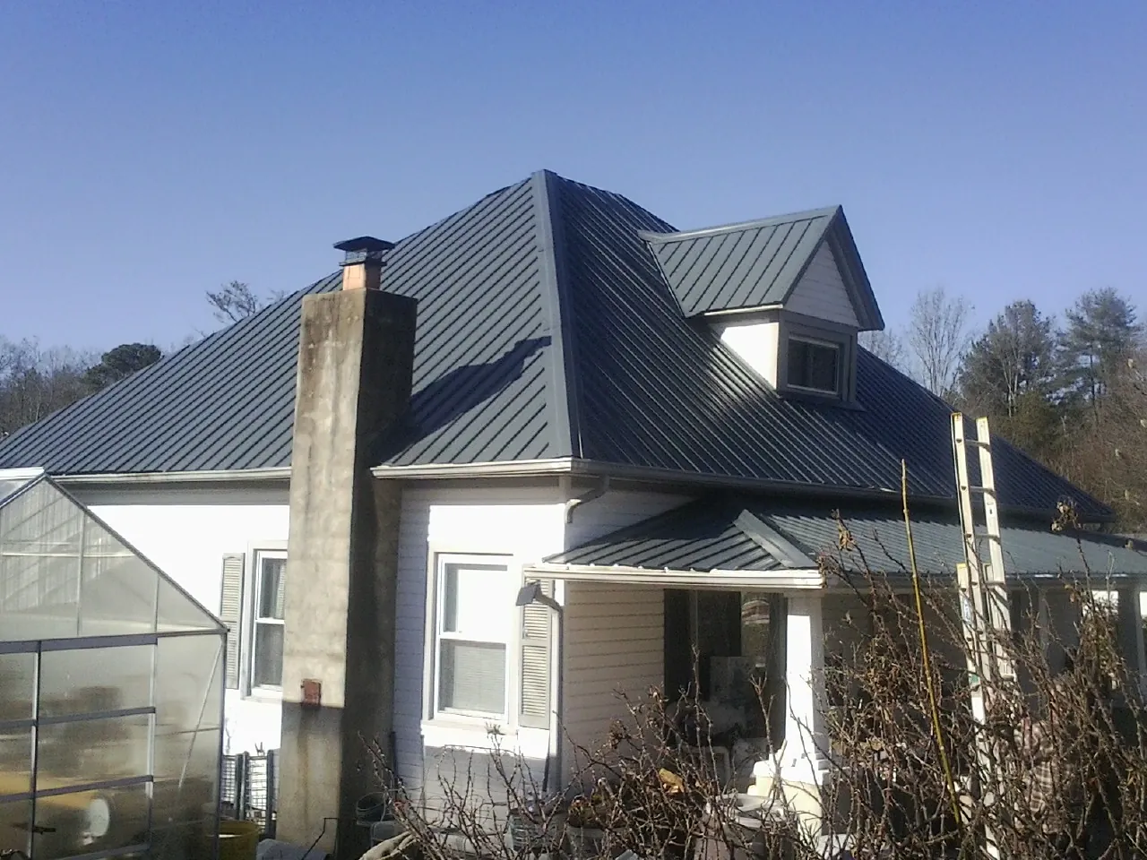 Dark blue standing seam metal roof on a white farmhouse with dormer — Slate & Tile Roof Repair by Roofing Brothers in Briggs