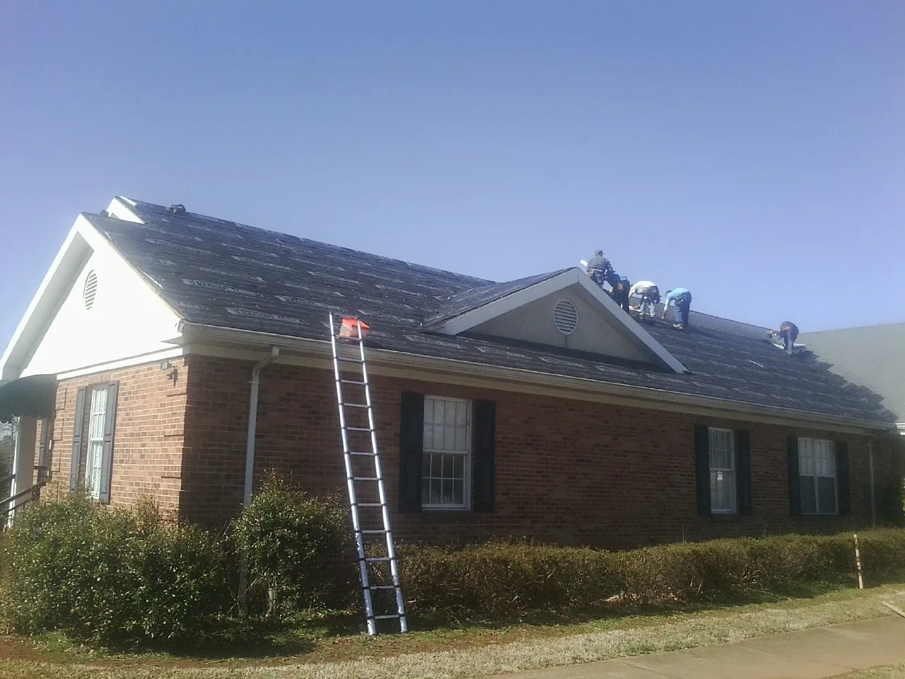 Crew tearing shingles off a brick ranch roof with a ladder set — Metal Roof Repair work by our crew in Briggs