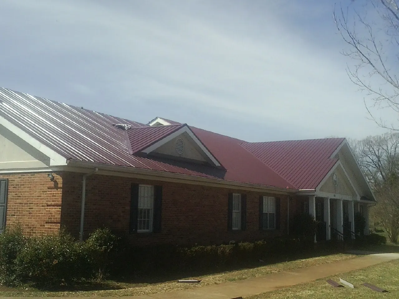 Red metal roof with gabled entries on a long brick building, from a Hail Damage Roof Repair job in Briggs