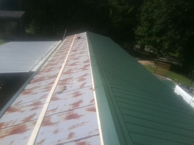 Old rusted panels beside newly installed green metal roofing — Wind Damage Roof Repair by Roofing Brothers in Briggs