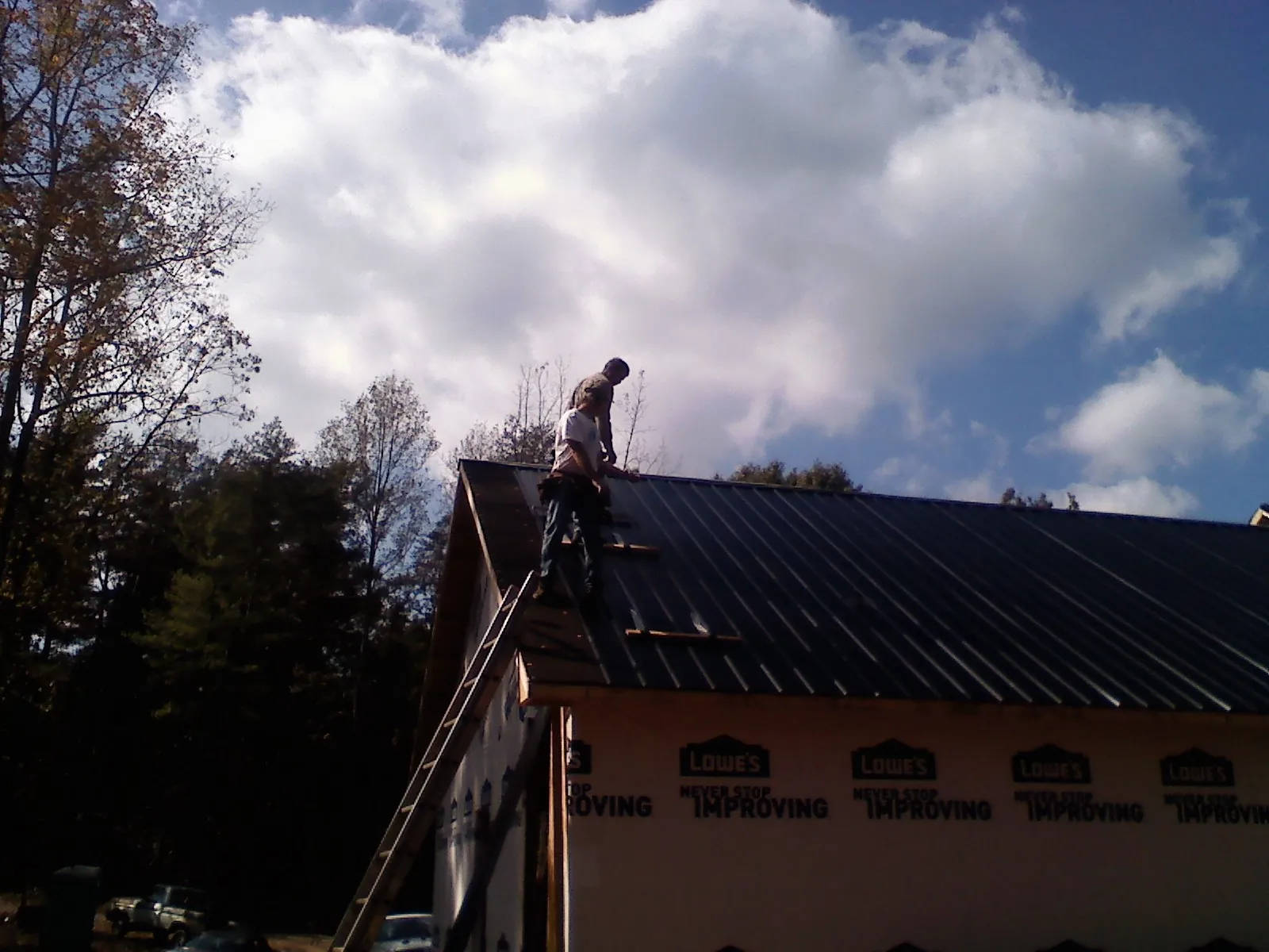 Roofer fastening dark metal panels high against a cloudy sky, from a Roof Inspection job in Briggs