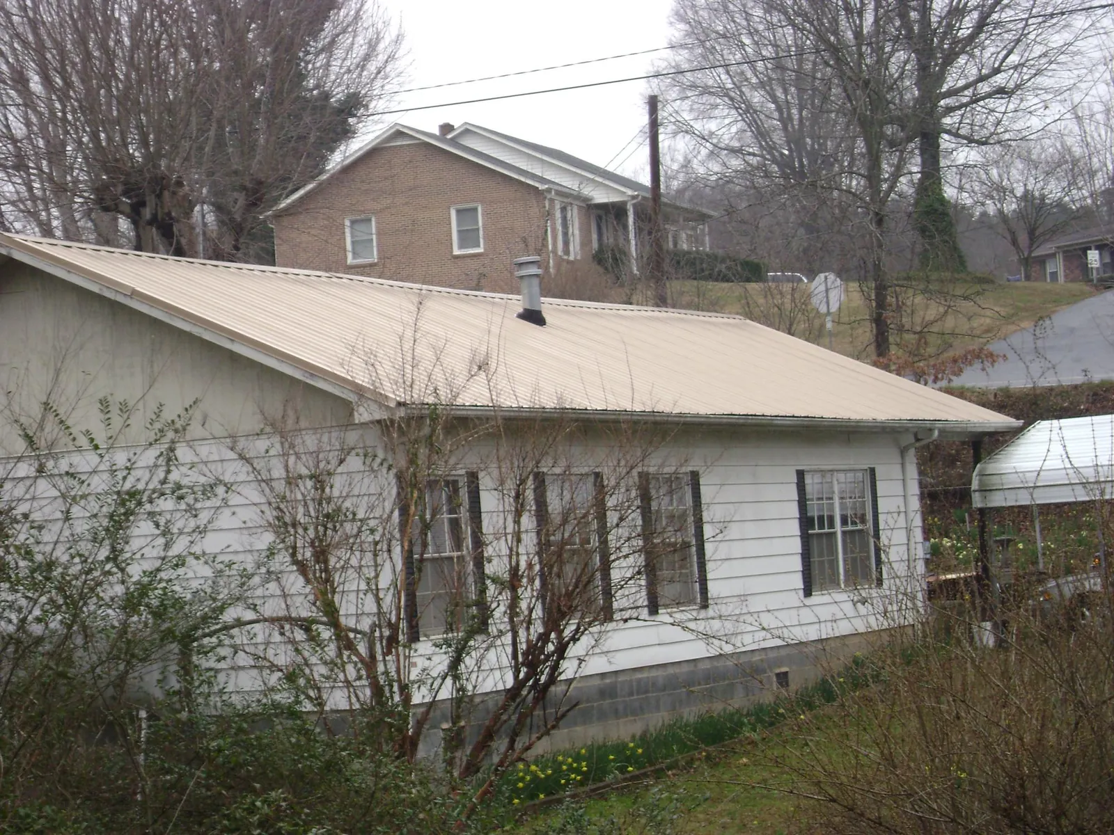 Tan metal roof on a white sided house set into a hillside — Commercial Roofing by Roofing Brothers in Briggs