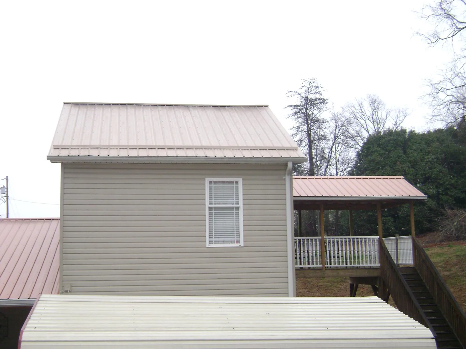 Tan metal roofs on a two story addition and attached porch, from a Roof Replacement job in Briggs